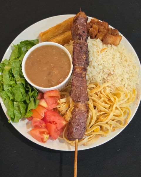 Plate with a grilled beef skewer, beans, rice, pasta, lettuce, tomato, fried cassava and torresmo