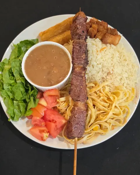 Plate with a grilled beef skewer, beans, rice, pasta and salad
