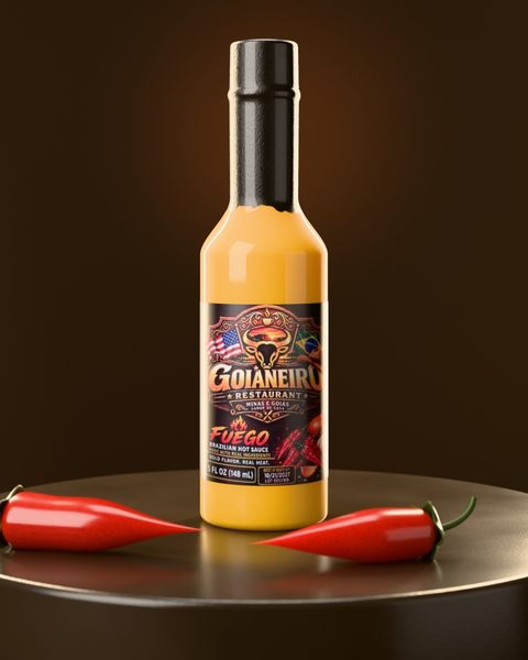 Bottle of Goianeiro Fuego Brazilian Hot Sauce on a dark stone pedestal with two red chili peppers